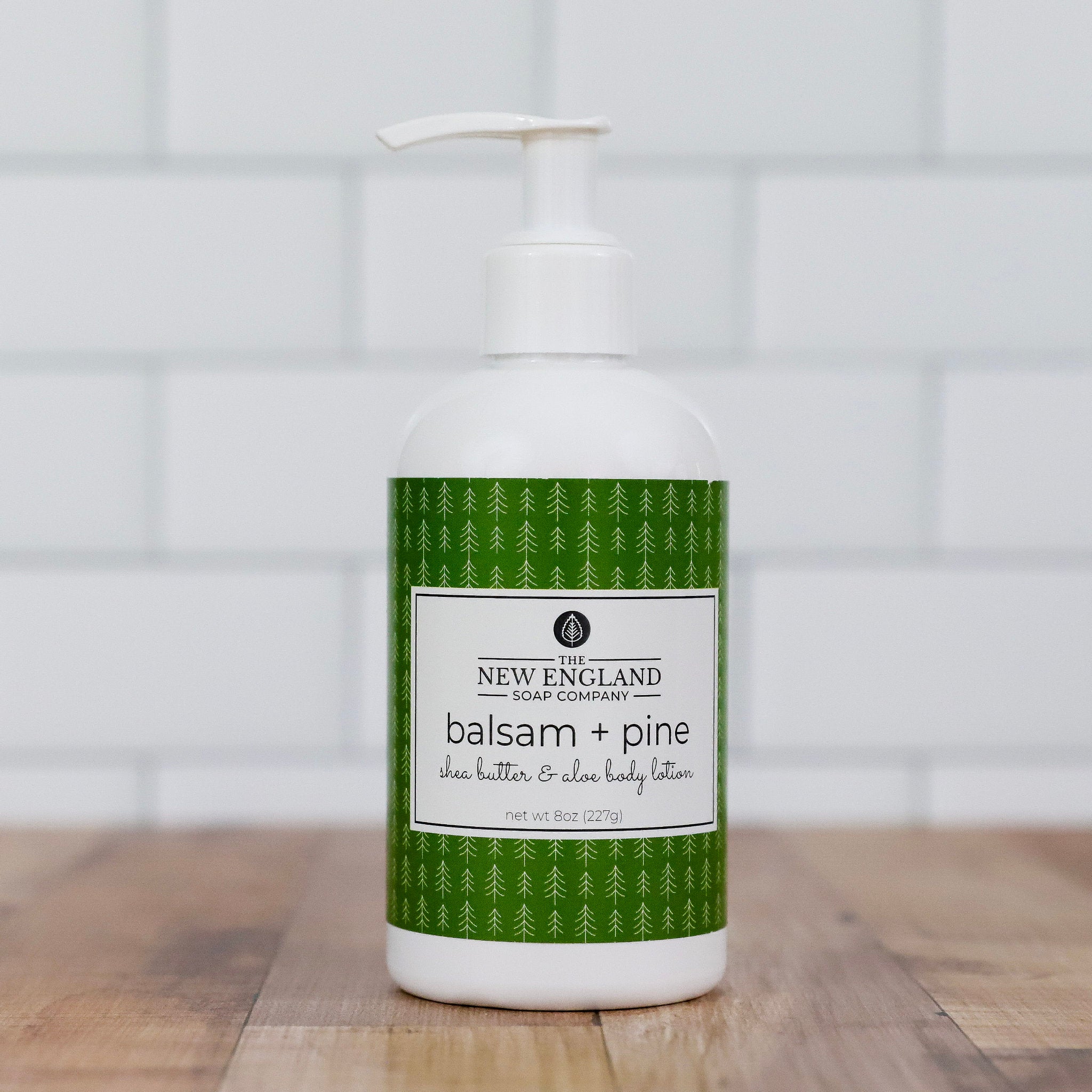 Bottle of New England Soap Company balsam and pine body lotion on a wooden surface with a tiled wall background.