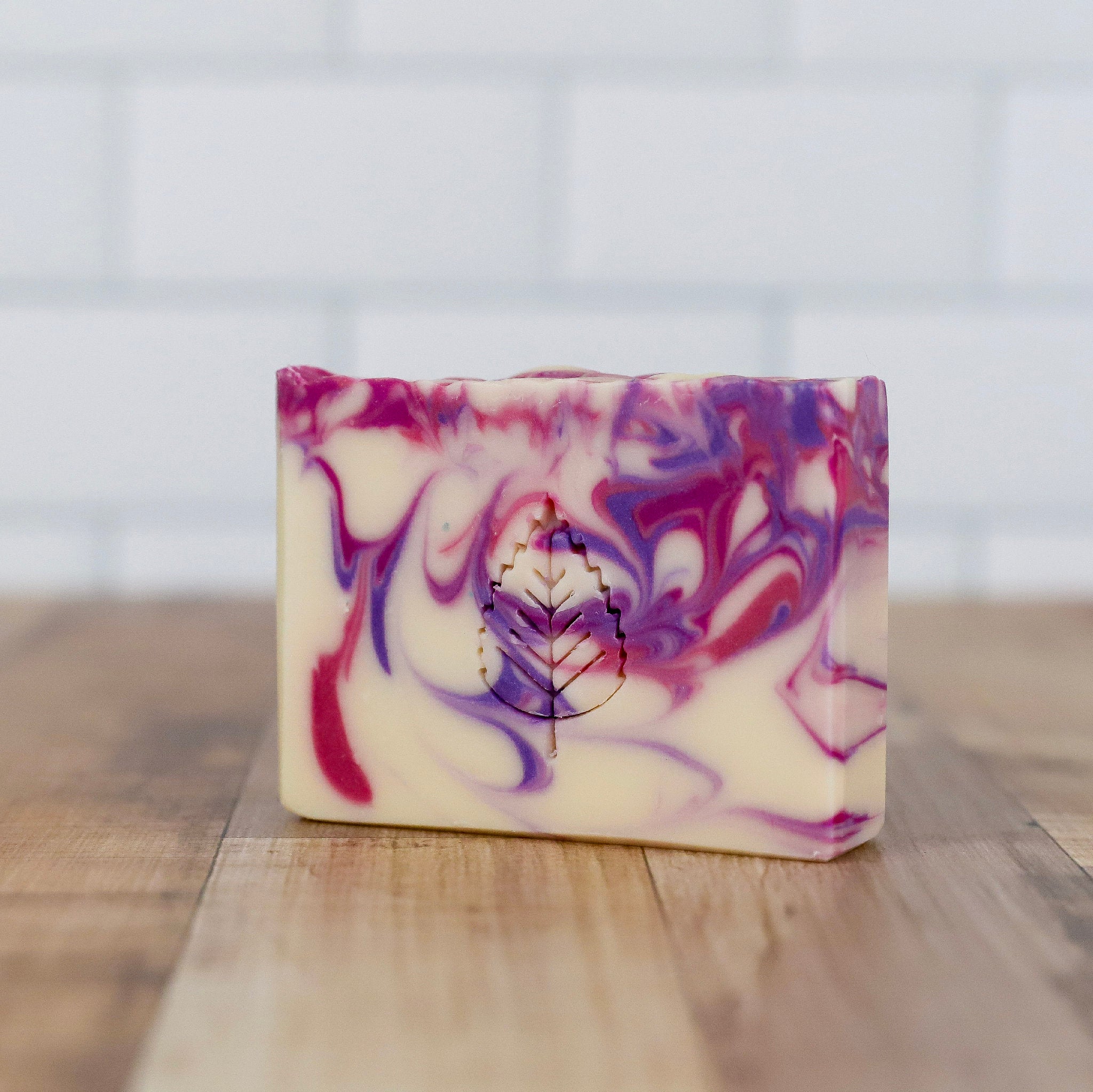 Marbled purple and pink soap bar on a wooden surface with a white background