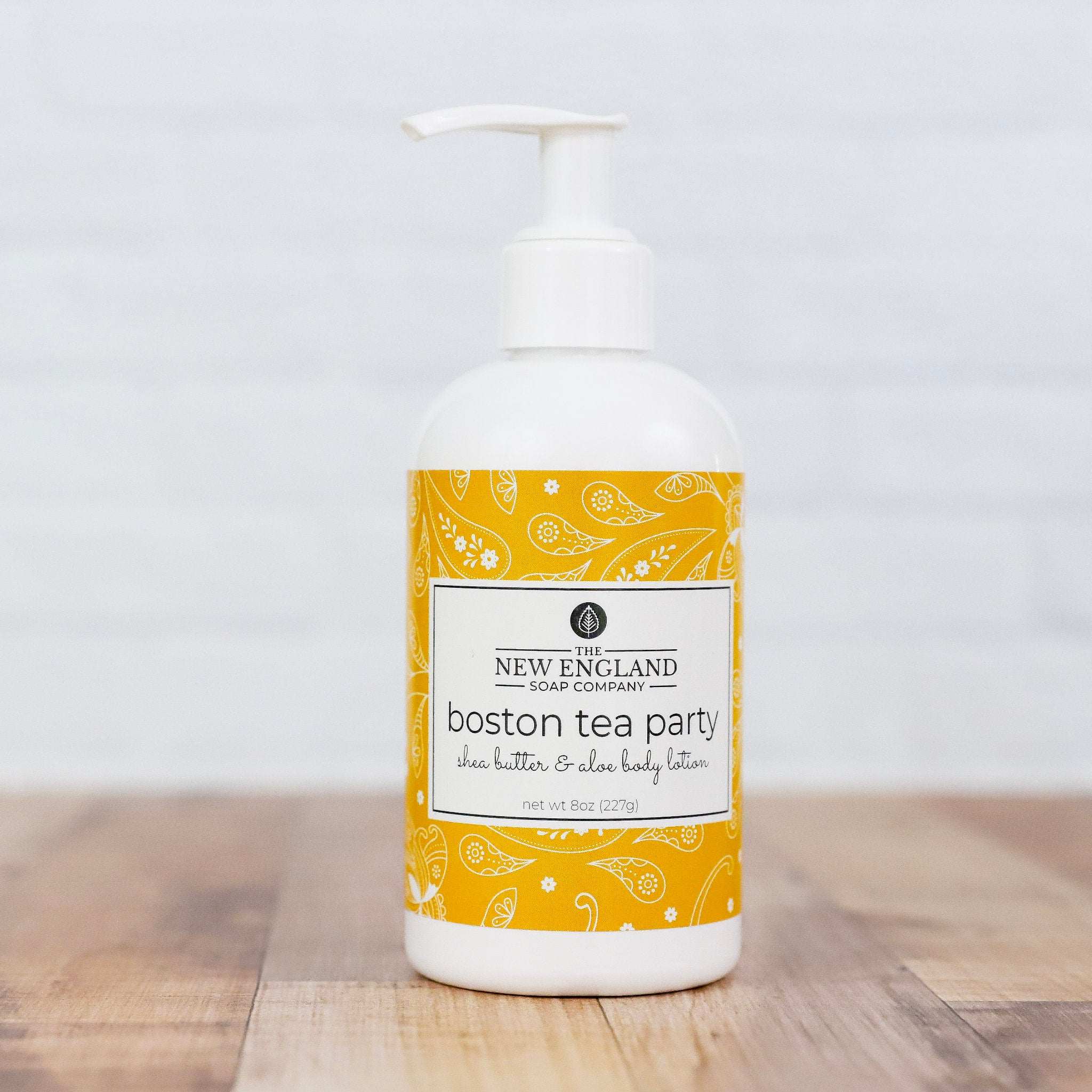 Body lotion bottle with yellow and white label on a wooden surface Boston Tea Party Hand and Body Lotion 8 oz