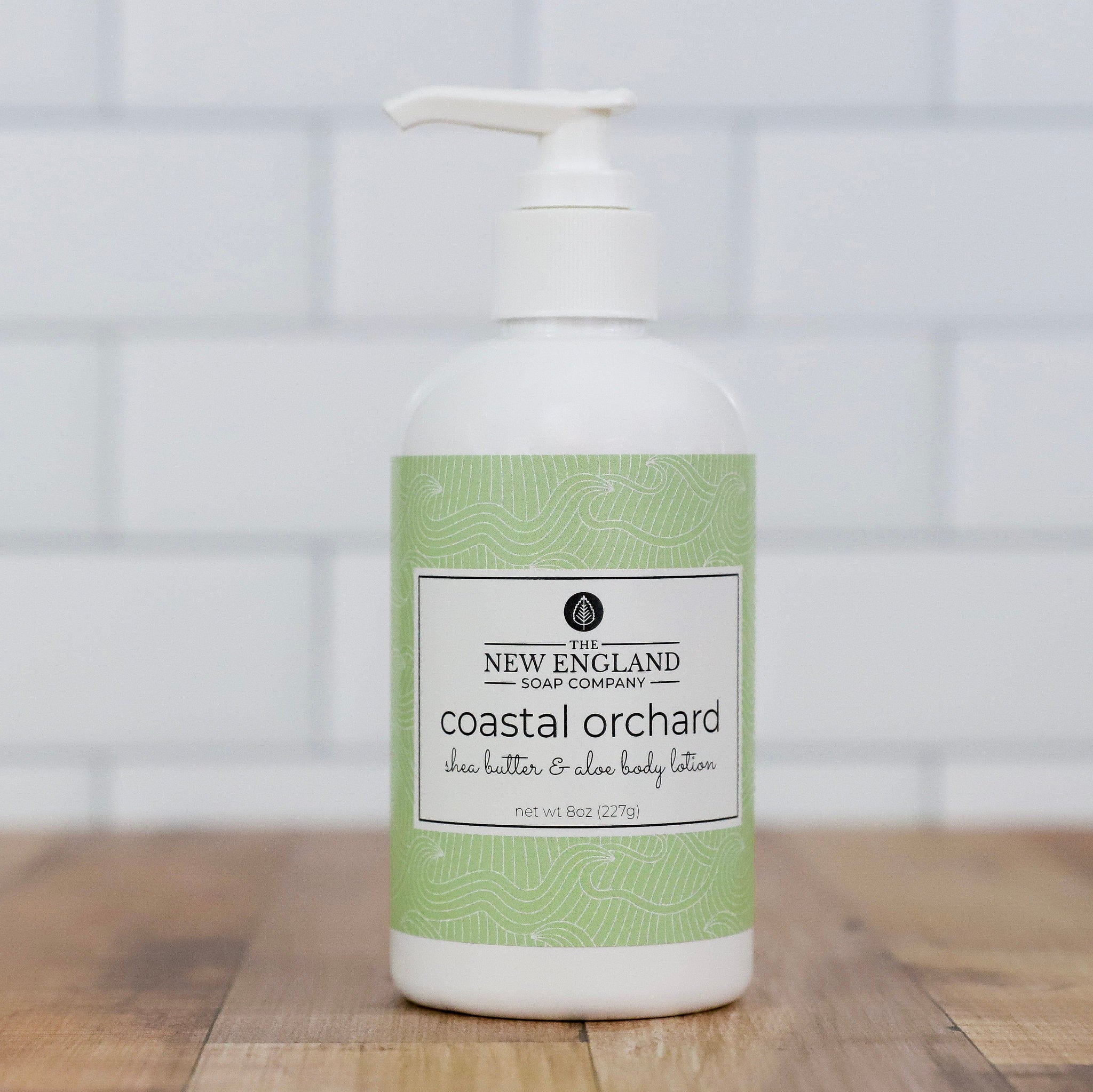 Body lotion bottle with green label on a wooden surface and tiled wall Coastal Orchard Hand and Body Lotion 8 ozbackground