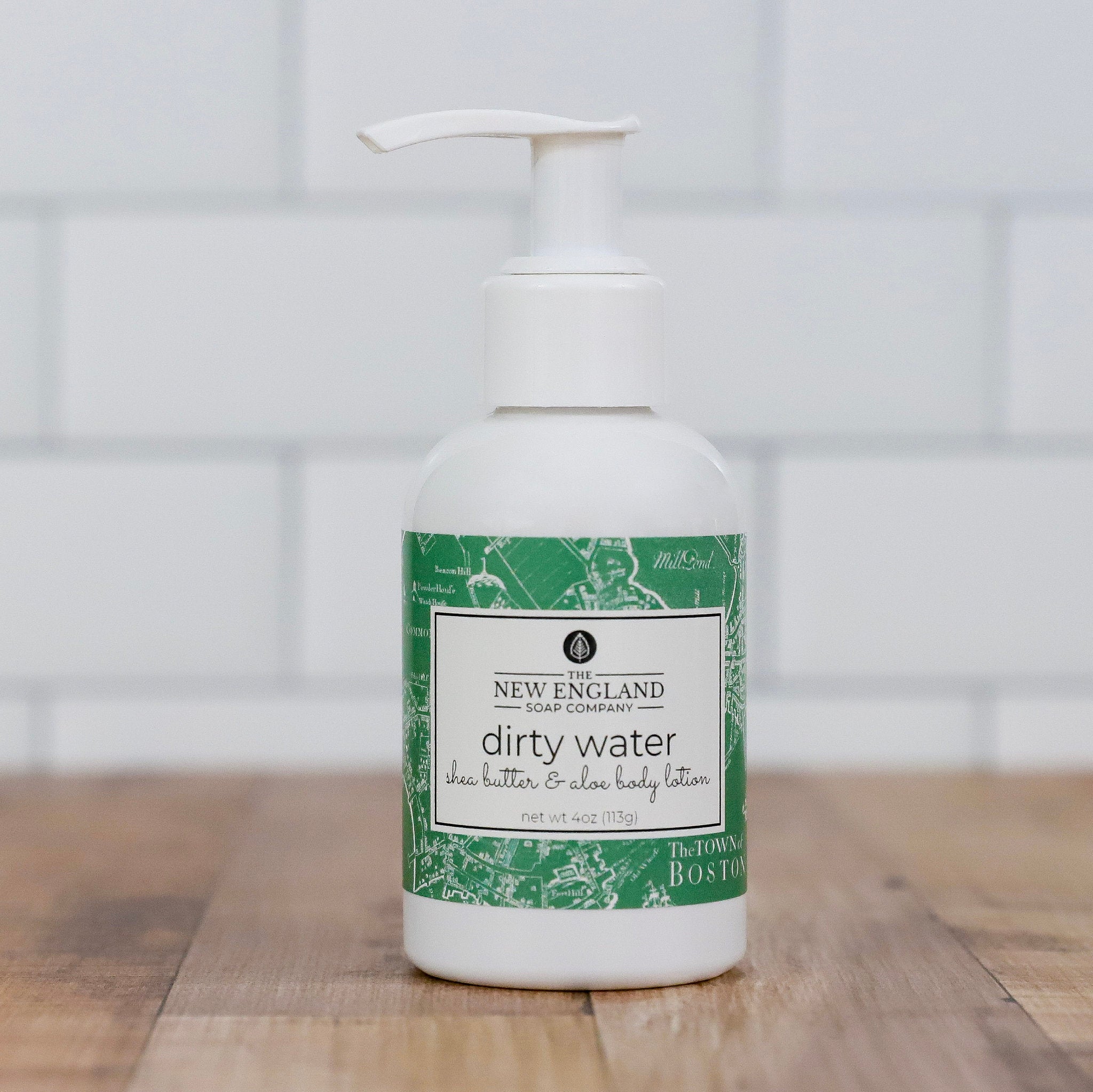 Body lotion bottle with green and white label on a wooden surface Dirty Water Hand and Body Lotion 4 oz