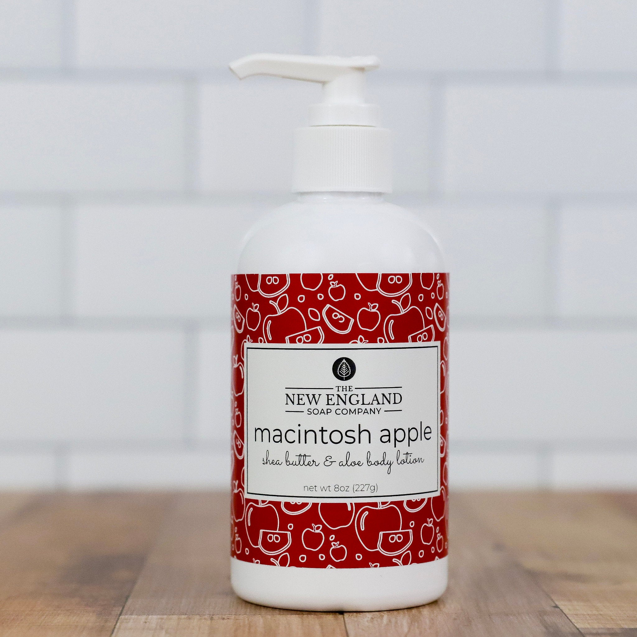 Bottle of New England Soap Company macintosh apple lotion on a wooden surface with a tiled wall background Macintosh Apple Hand and Body Lotion 8 oz