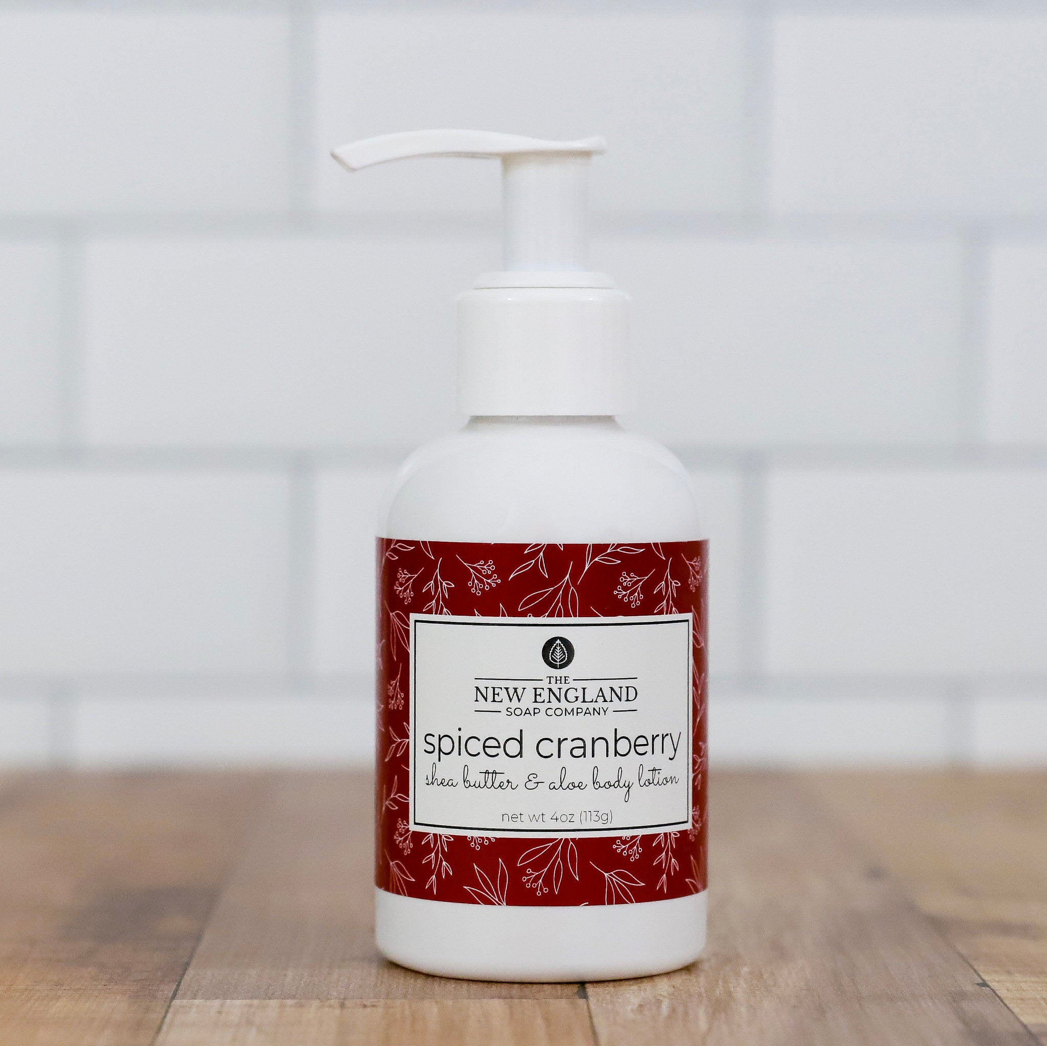 Spiced cranberry body lotion bottle with a white pump on a wooden surface.