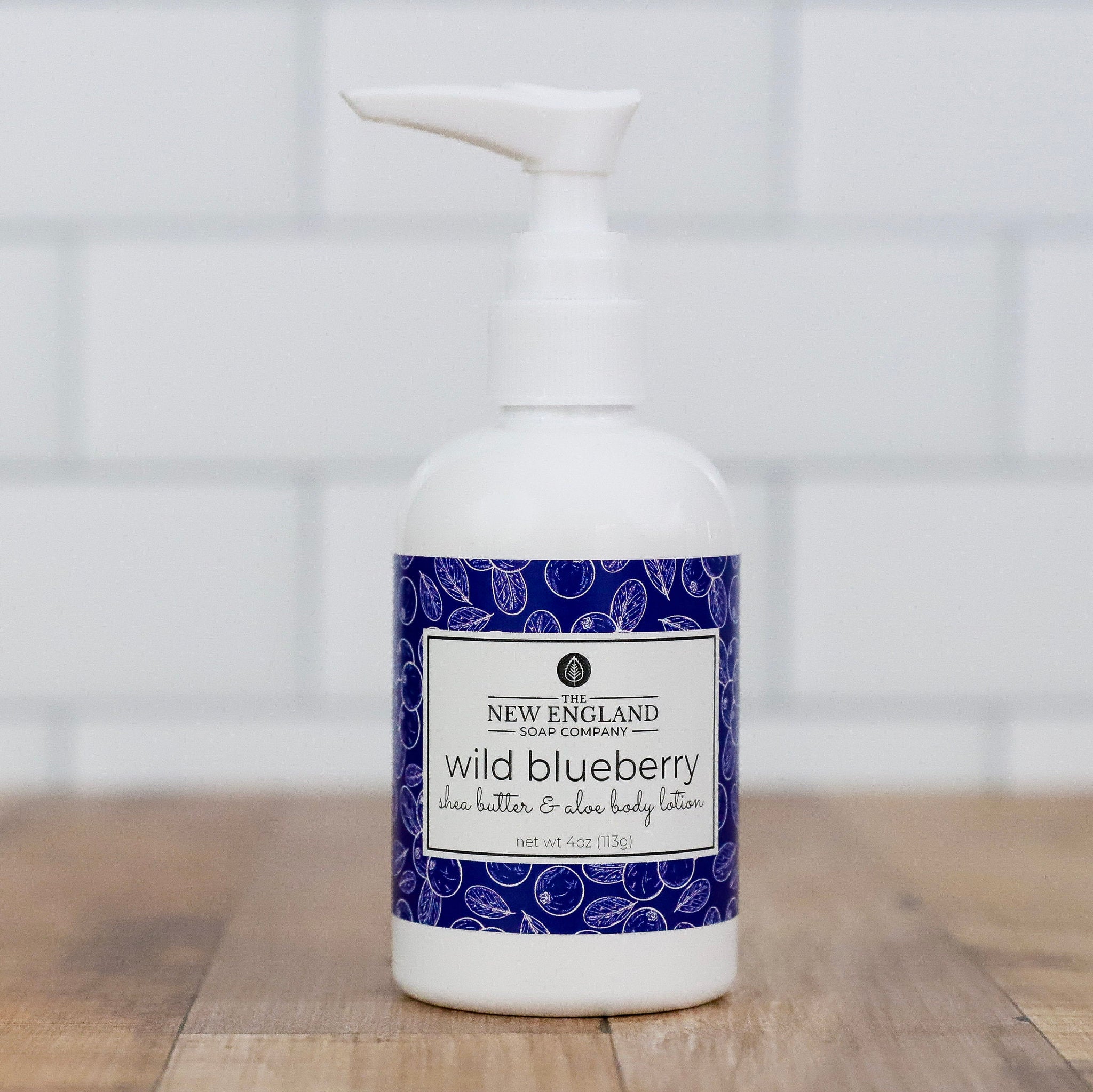 White bottle of New England Soap Company wild blueberry lotion on a wooden surface with a white background Wild Blueberry Hand and Body Lotion 4 oz