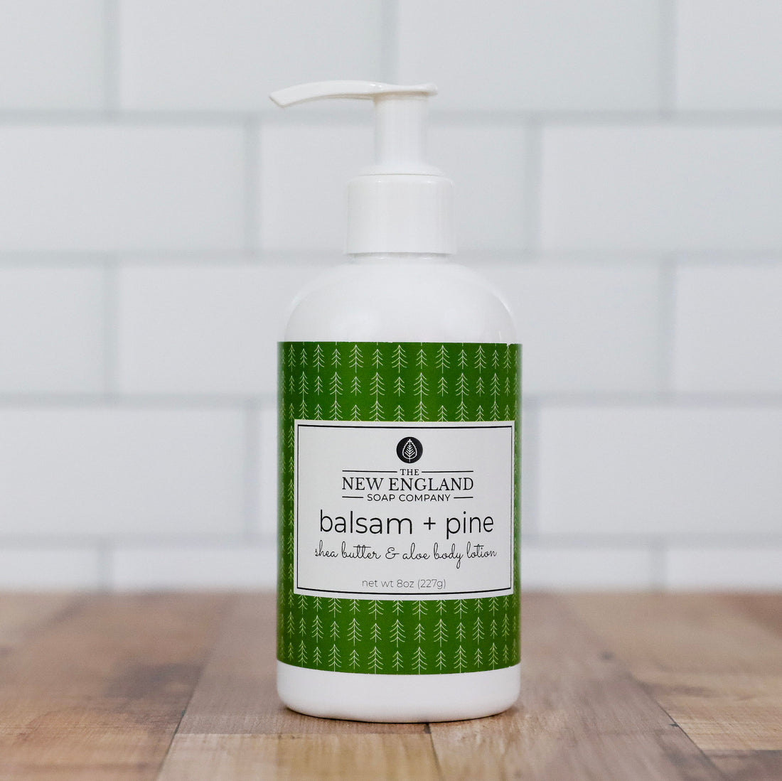 Bottle of New England Soap Company balsam and pine body lotion on a wooden surface with a tiled wall background.
