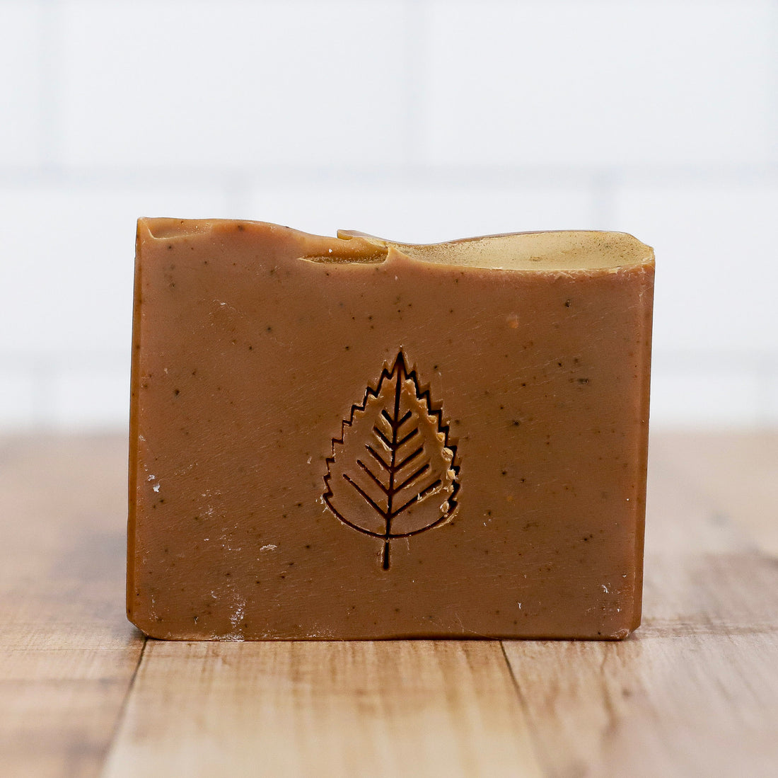 Brown bar of soap with a leaf impression on a wooden surface