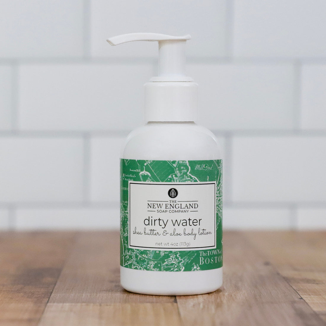 Body lotion bottle with green and white label on a wooden surface Dirty Water Hand and Body Lotion 4 oz