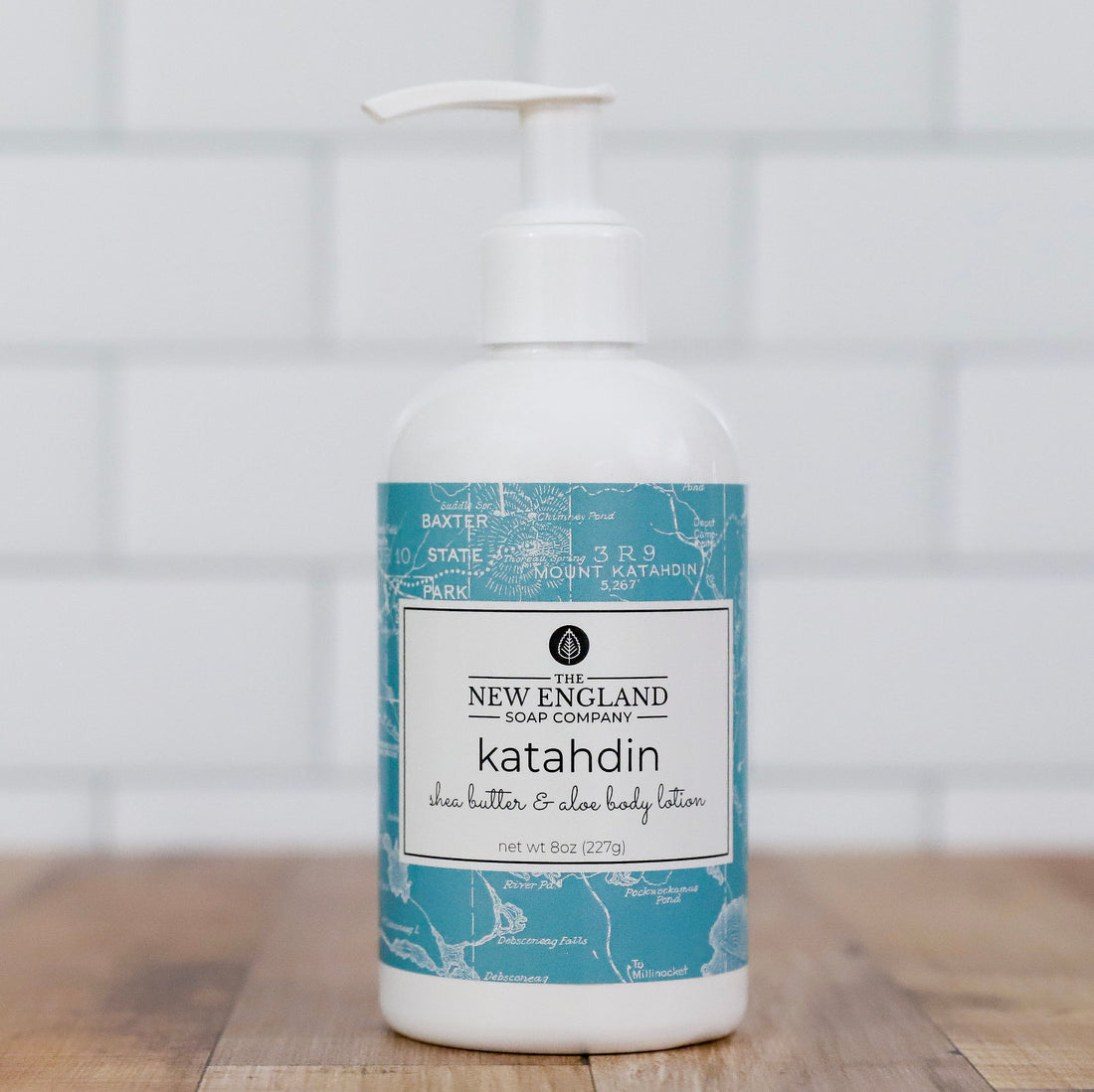 New England Soap Company Katahdin shea butter &amp; aloe body lotion on a wooden surface with a tiled wall background Katahdin Hand and Body Lotion 4 oz