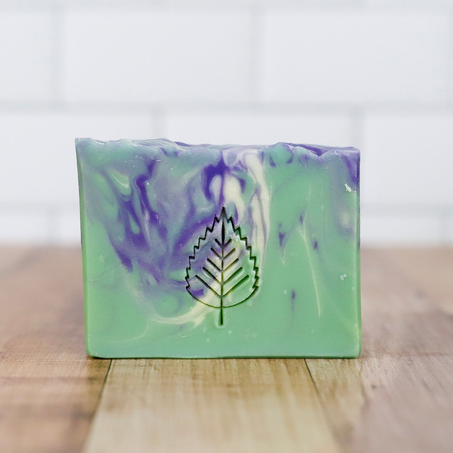 Green and purple soap bar with a leaf logo on a wooden surface