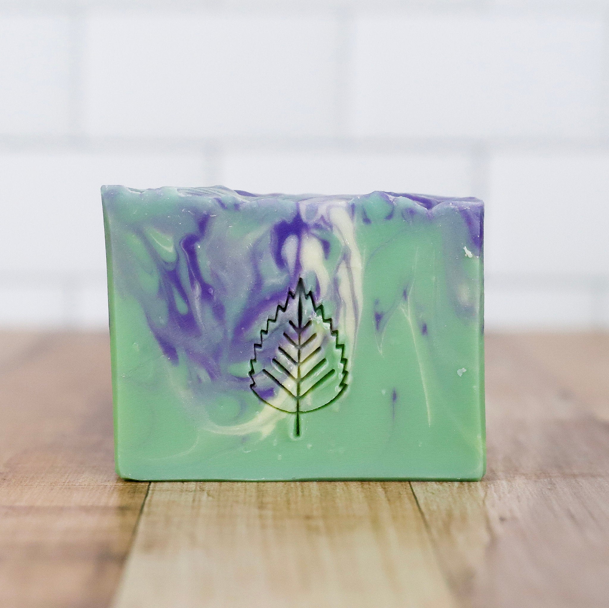Green and purple soap bar with a leaf logo on a wooden surface