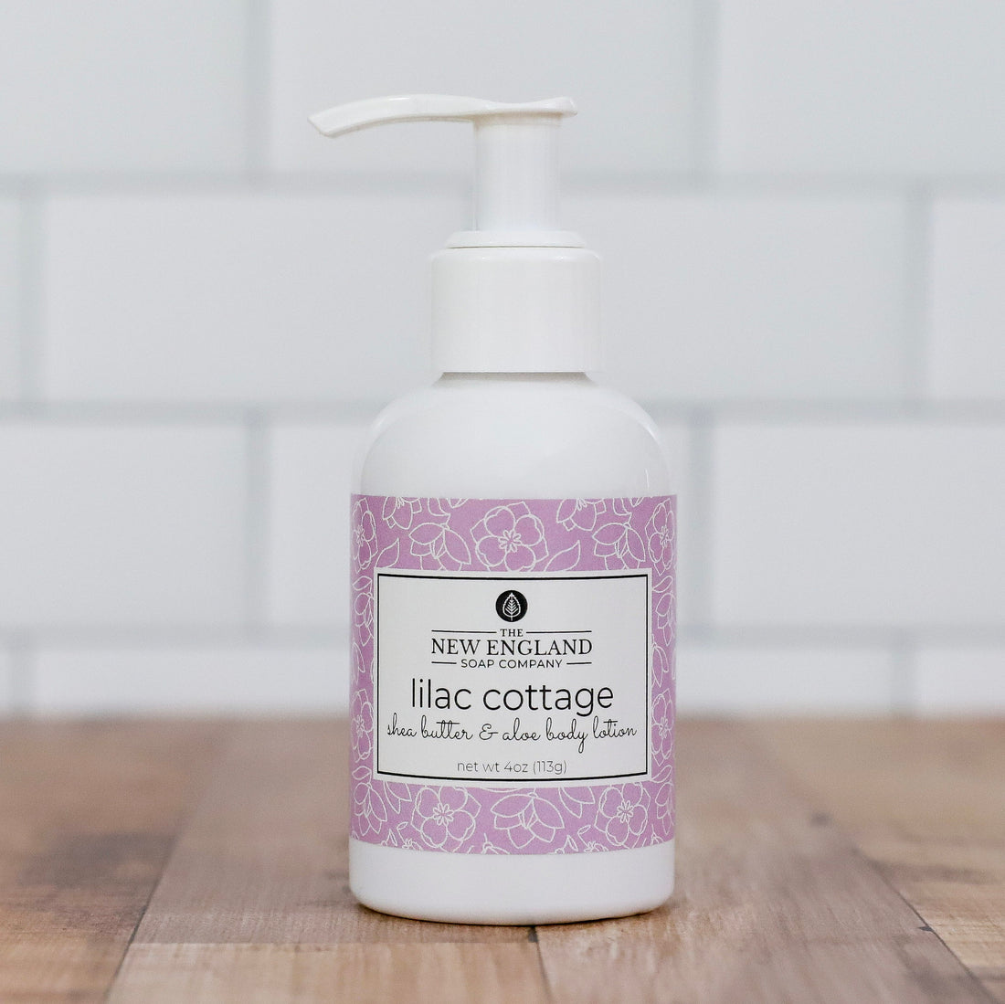 Lilac cottage body lotion bottle on a wooden surface with a white tiled wall background