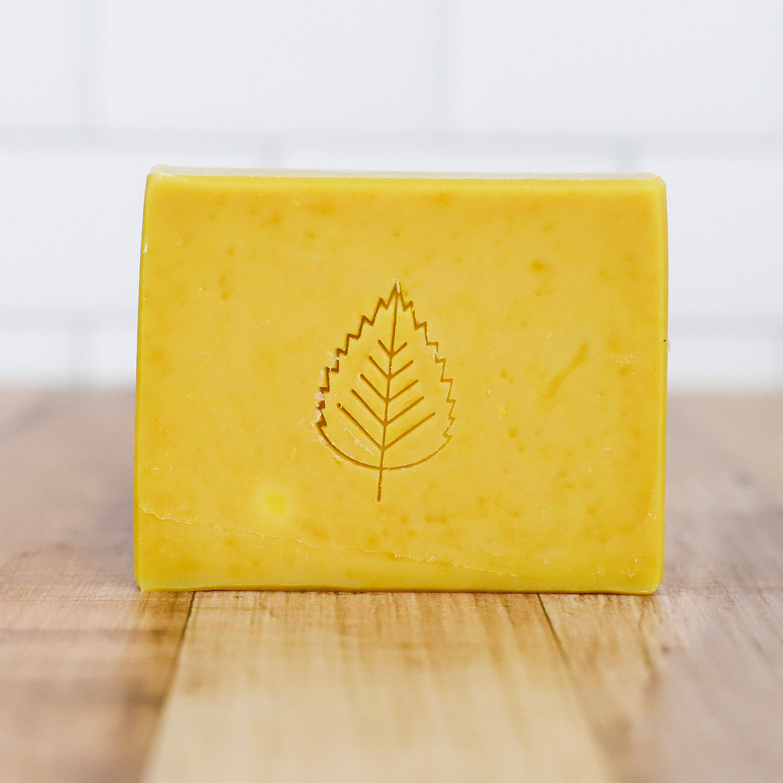 Yellow bar of soap with a leaf design on a wooden surface Poets and Philosophers Artisan Soap
