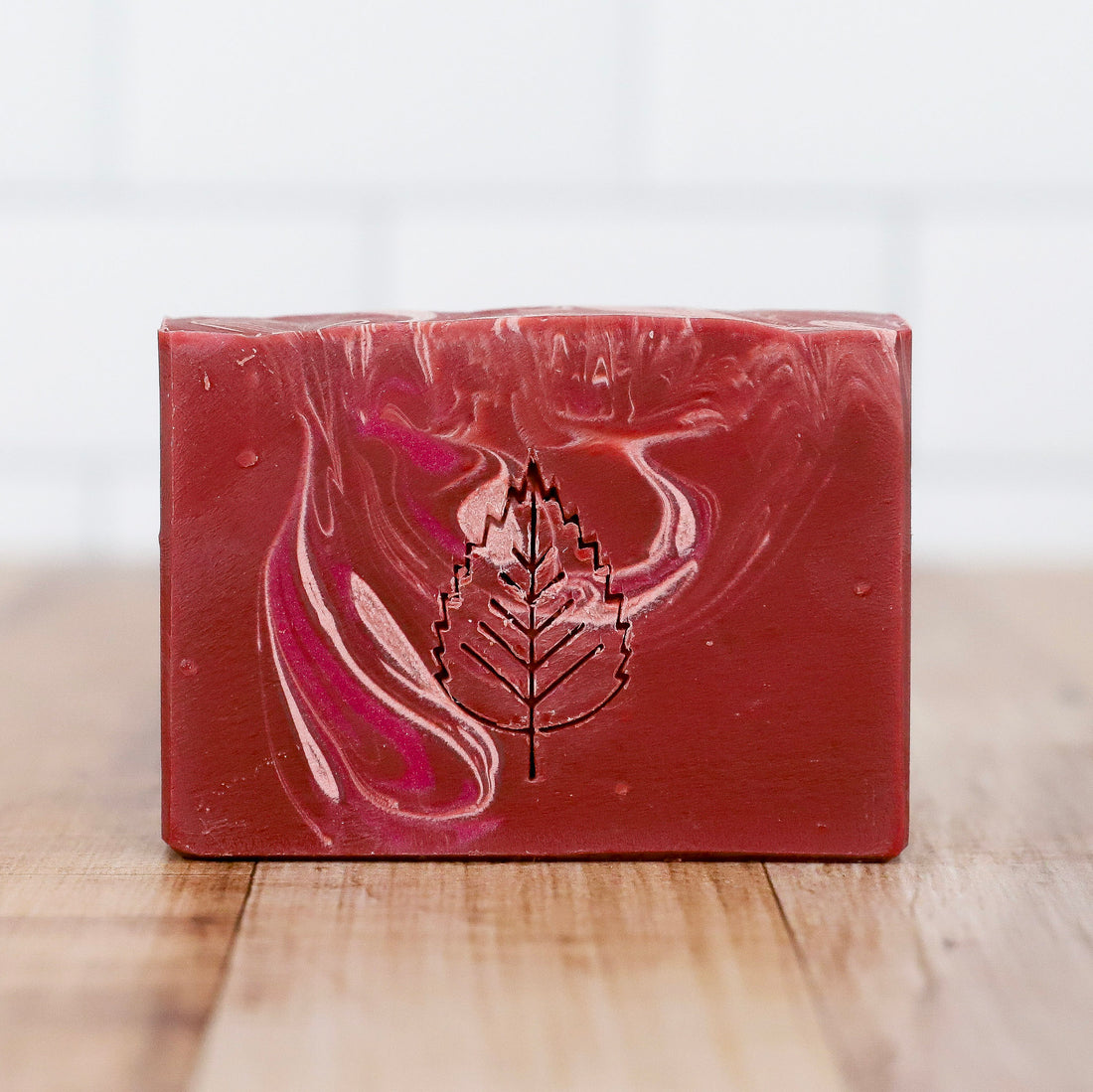 Marbled red and white soap bar with a leaf logo on a wooden surface