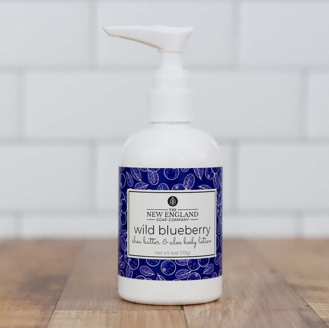 White bottle of New England Soap Company wild blueberry lotion on a wooden surface with a white  background Wild Blueberry Hand and Body Lotion 4 oz
